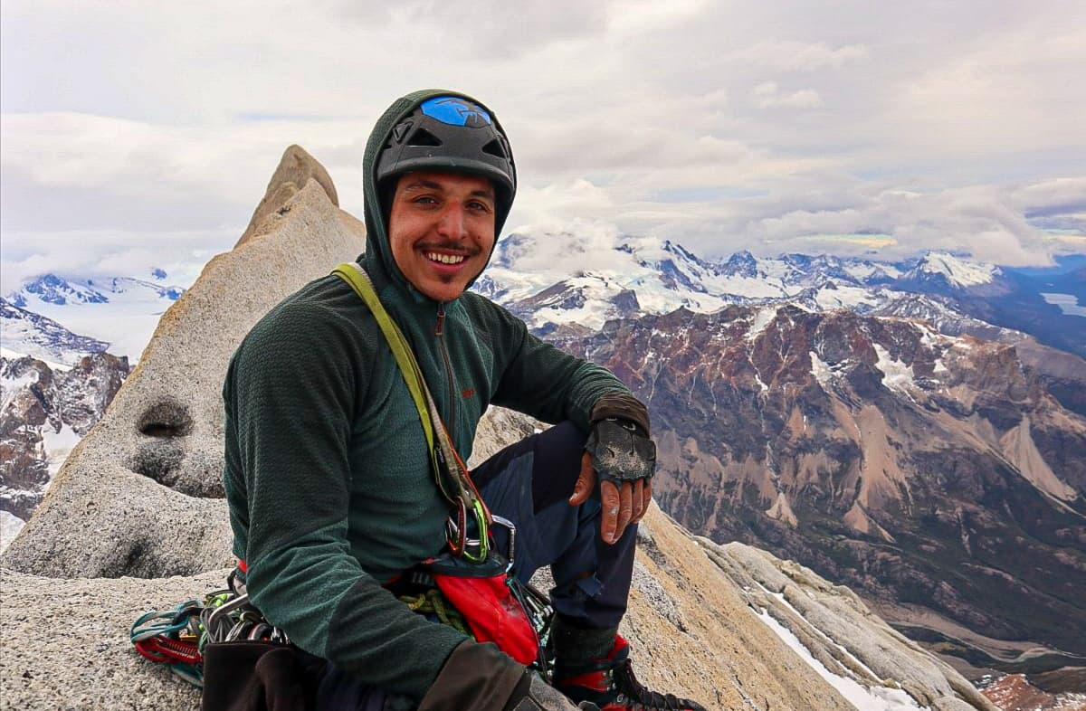 Joaquín Cisterna wearing a climbing helmet on a granite summit above Patagonian mountains.